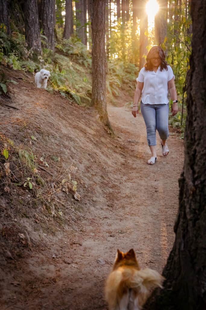 Maha Elias walking on a path with her dogs. Sun behind her.